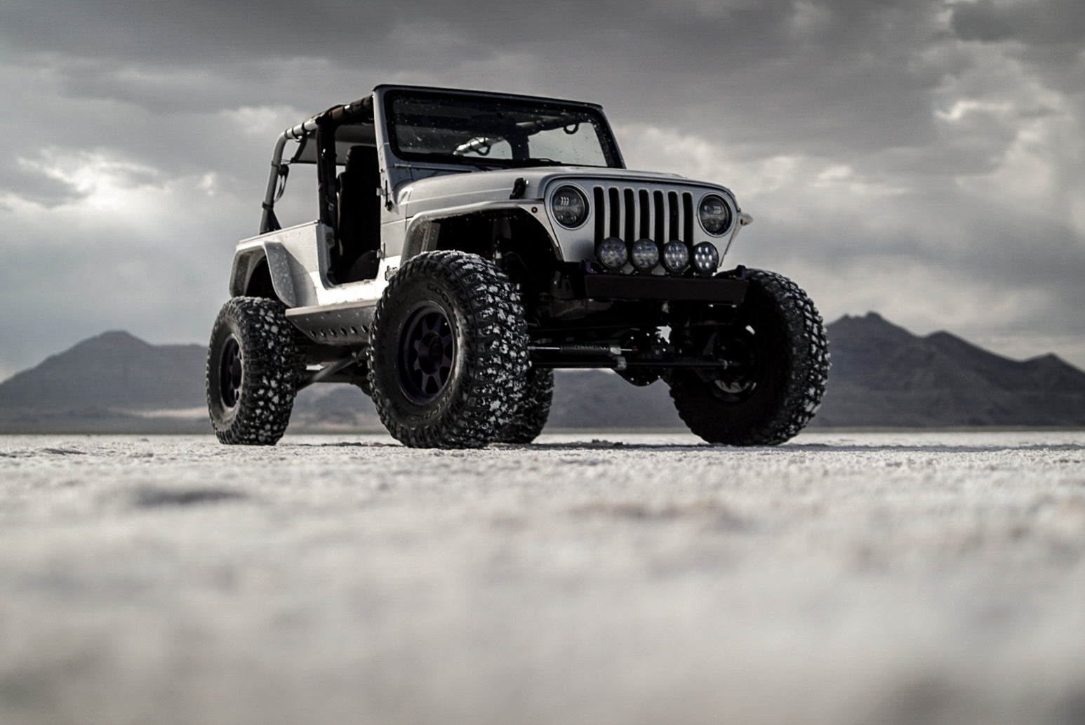 Silver Jeep Wrangler on a desert landscape with mountains in the background